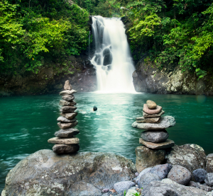 Tropischer Wasserfall auf Bali mit Naturbecken und Steinfiguren im Vordergrund.
