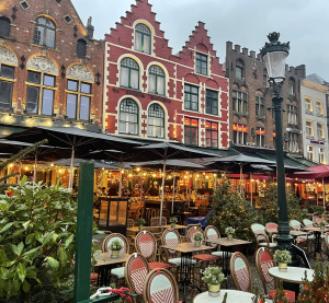 Außengastronomie auf einem Platz vor historischen Giebelhäusern in Brügge, Belgien, mit gedeckten Tischen und Pflanzen.
