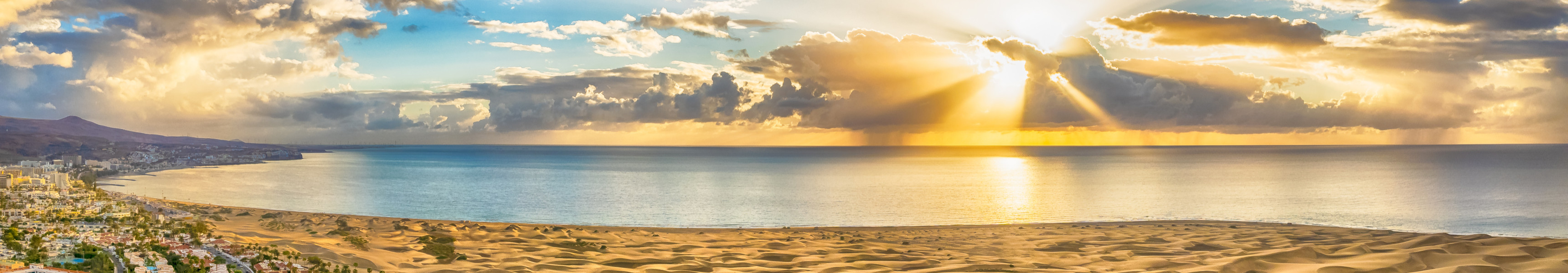 Sonnenuntergang &uuml;ber den D&uuml;nen von Maspalomas mit Blick auf das Meer und Hotels auf Gran Canaria.