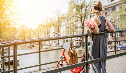 Frau mit Blumenstrau&szlig; lehnt an einem Br&uuml;ckengel&auml;nder in Amsterdam, neben ihr ein rotes Fahrrad.