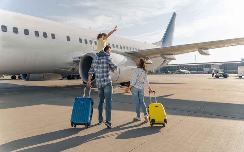 Familie l&auml;uft mit Koffern zum Flugzeug und das Kind sitzt auf den Schultern des Papas. 